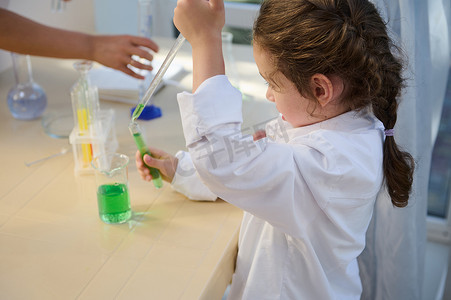 聪明孩子使用刻度移液器和测量玻璃器皿在学校化学实验室做实验的侧视图