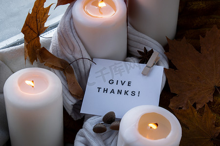 氛围灯光摄影照片_给予感谢文字贺卡概念在舒适的家中在窗台上庆祝感恩节秋季假期Hygge美学氛围秋叶香料和蜡烛在针织白色毛衣上温暖的黄色灯光。