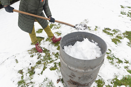 水在自然界的循环摄影照片_中年妇女正在用铲子在桶里收集雪，自然资源