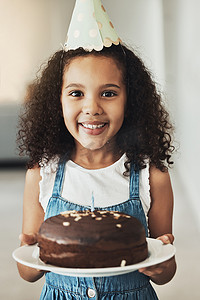 生日蛋糕帽子摄影照片_快乐的女孩拿着生日蛋糕，在家里与孩子合影，独自在亚特兰大的房子里进行惊喜庆祝。