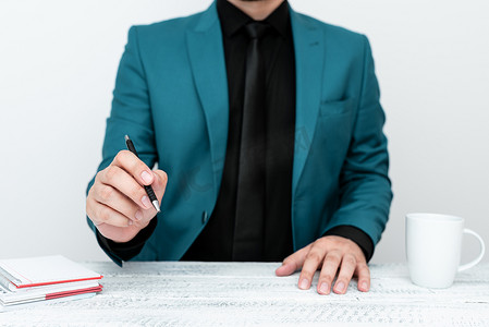 身穿蓝色西装的男模特坐在白色桌子旁，用笔指着重要信息。