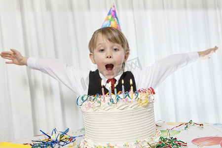 年轻的生日戴着派对帽，张开双臂在蛋糕上吹蜡烛