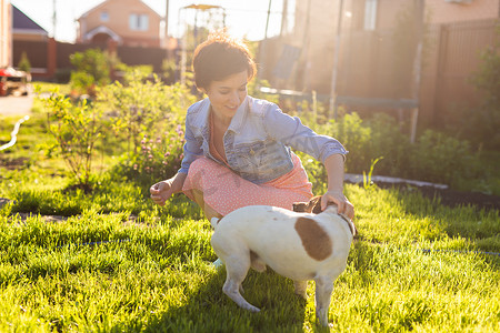 宠物狗玩耍摄影照片_年轻女子在后院的草地上和她的狗玩耍。