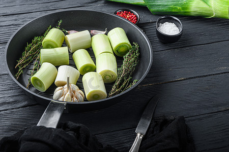 烤韭菜摄影照片_生炖韭菜苏丹在烤盘上，未用香草成分煮熟，在黑色木桌侧视图上，有文字空间。