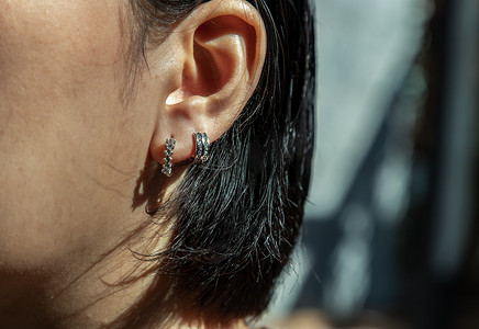 银耳环摄影照片_戴着美丽的银耳环的年轻女子的细节。