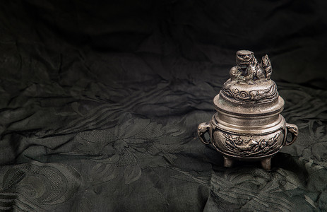 雕刻装饰在深色背景上的小银色古代香炉上。