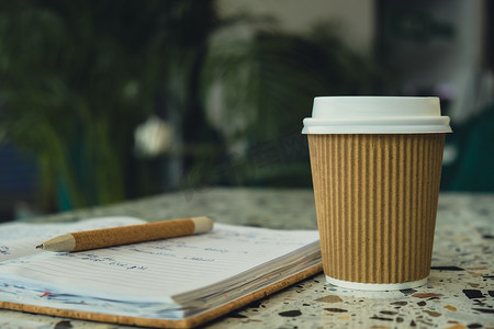 工艺回收纸杯中的热拿铁咖啡和纸质笔记本。