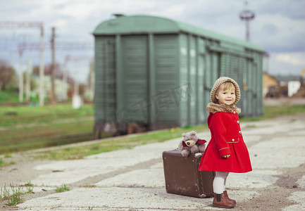 一件红色外套的迷人的婴孩带着手提箱正在等待火车