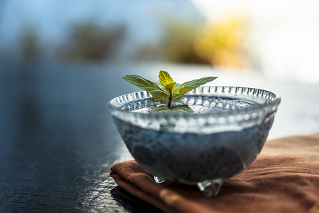 将浸湿的 sabja 种子或法卢达种子或甜罗勒种子放在玻璃碗中，放在木质表面的棕色餐巾上，里面有一些薄荷叶。用于许多风味饮料。