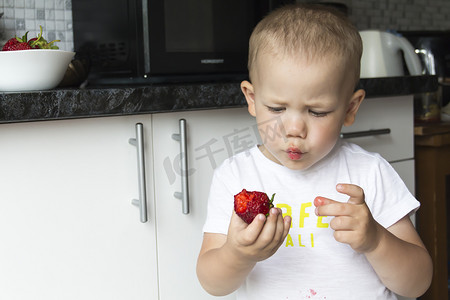 不合摄影照片_一个秃顶的小男孩正在不整齐、不合胃口地吃着红红多汁的草莓。