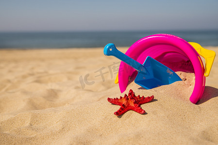 塑料桶摄影照片_阳光明媚的海滩上的玩具