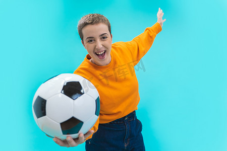 尖叫的年轻女子足球迷穿着橙色毛衣，与蓝色背景隔离。