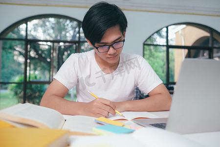 年轻的亚洲男学生正准备阅读大学考试的书籍。