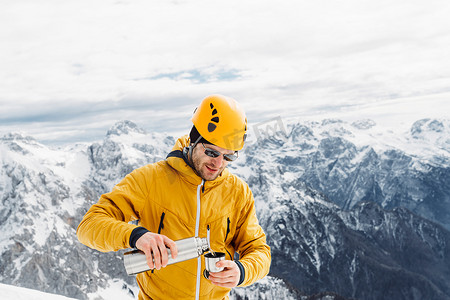 生活是自己的摄影照片_穿着黄色夹克和头盔的登山者给自己倒了一些茶，背景是白雪皑皑的阿尔卑斯山