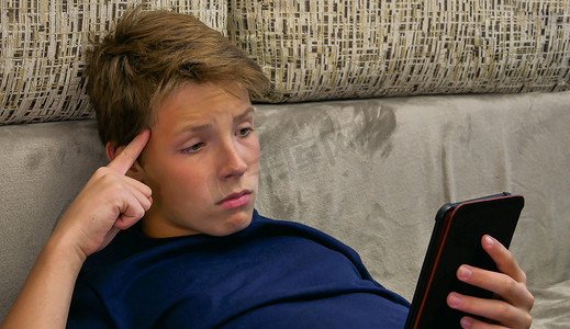 不满意和惊讶的男孩阅读电子设备。