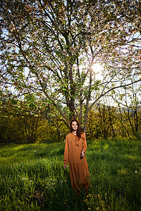 一位甜美、谦虚的长发女士站在乡村，靠近一棵开花的树，双手紧握在一起看着镜头