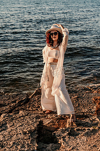 一个穿着白色裤装、戴着帽子的女人站在海滩上享受大海。