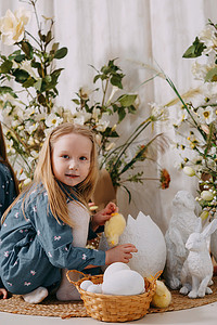 两个女孩在一个美丽的复活节拍照区，里面有鲜花、鸡蛋、鸡和复活节兔子。