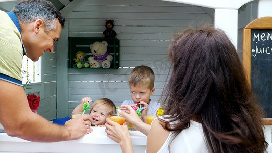 鲜榨果汁广告摄影照片_夏天，花园里，父母爸爸妈妈提着鲜榨果汁给孩子们吃。