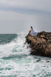 海中石头摄影照片_暴风雨中的一个女人坐在海中的一块石头上。