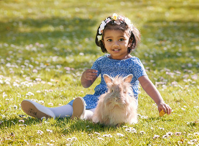 一个亚洲小女孩正和家兔坐在绿草上
