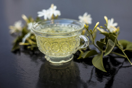 印度茉莉花茶或 Juhi 或 Jasminum Auriculatum 茶的特写，在玻璃杯的木质表面上，上面有生花。
