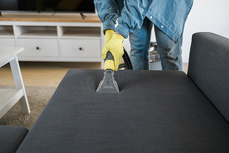 戴防护橡胶手套的男子用专业提取方法用清洗吸尘器清洁沙发。