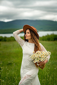 一名身穿白色连衣裙、棕色帽子的中年妇女抱着一名身穿白色连衣裙、棕色帽子的中年妇女，她手里拿着一个篮子，里面放着一大束雏菊。她手里拿着一大束雏菊。
