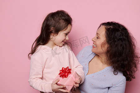 快乐的母女一起玩得很开心，微笑，拥抱，在孤立的粉红色背景上摆着可爱的礼物
