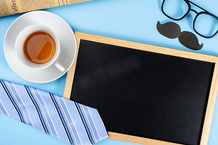 快乐父亲节背景概念，配有蓝色领带眼镜、报纸、黑胡子、一杯茶和蓝色背景的黑板，带有文本复制空间。