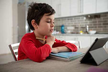 专注的男生在家里的在线课堂上使用数字平板电脑。
