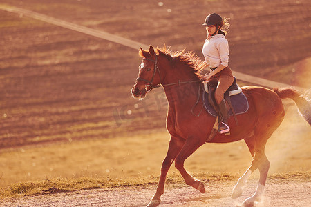 阳光明媚的白天，戴防护帽的年轻女子在农田里骑马