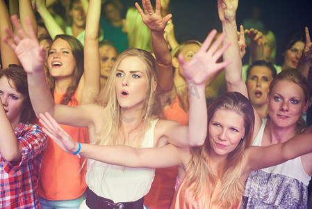 狂欢人群摄影照片_女性在音乐节、现场乐队表演和夜总会、音乐会和迪斯科舞厅的电子狂欢派对上举手跳舞。