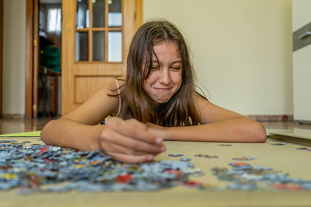 黑发少女躺在家里的地板上做拼图，她花时间逃离科技并享受传统游戏。