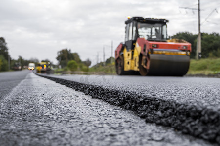 沥青道路摄影照片_带有重型振动压路机的沥青压路机在道路施工现场的巷道上压新的热沥青。