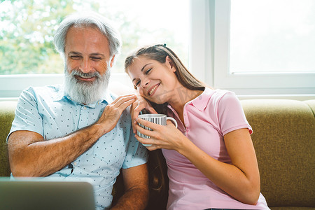 当他们看笔记本电脑上的照片时，微笑的年轻女子靠在祖父的肩膀上