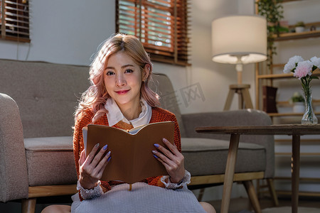 有魅力的年轻亚洲女性坐在简约舒适的客厅里享受读书。