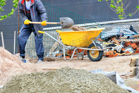 工人将沙子铲入黄色建筑独轮车。