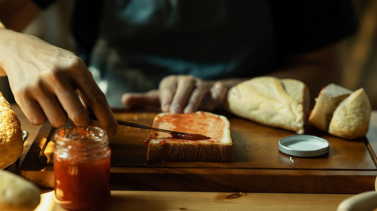 男人在厨房吃早餐或早午餐时，在面包上涂甜覆盆子果酱。