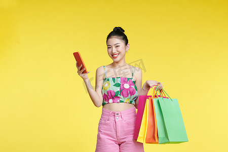 有魅力的亚洲微笑年轻女子拎着购物袋、手机