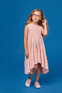 穿着粉色裙子、戴着眼镜的时尚小女孩站在蓝色背景上。