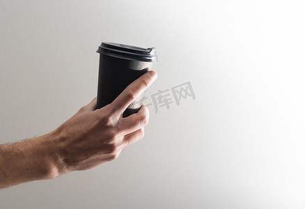 纸杯包装设计摄影照片_浅灰色背景下男性手持咖啡纸杯的模型