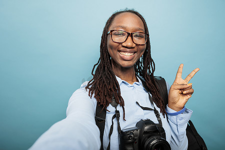 摄影爱好者摄影照片_积极快乐的摄影爱好者用单反相机用手指做和平标志