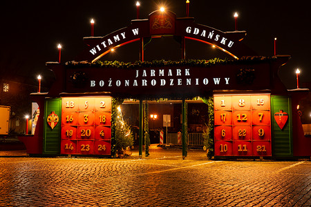 城市日历摄影照片_波兰格但斯克 — 2022年12月传统圣诞市场，配有大降临日历假日装饰和夜间照明的街道。