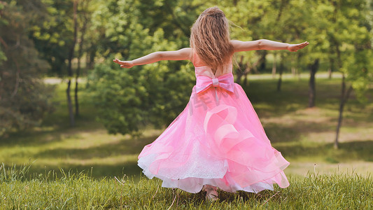 一个穿着粉色公主裙的女孩在公园里旋转。