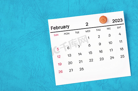 2023 年 2 月月历和蓝色背景上的木制图钉。