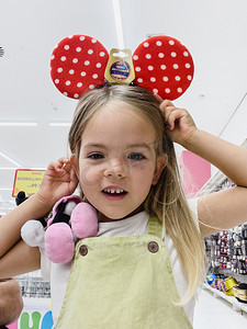 商店里的小女孩试戴可爱的红色圆点米妮老鼠耳朵
