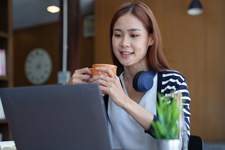 一位年轻、迷人的亚洲少女早上在图书馆上网学习时使用电脑、喝咖啡的肖像