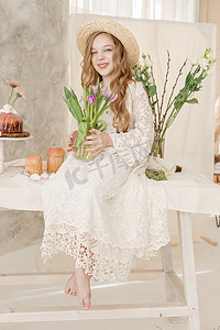 一个穿着裙子、戴着帽子、长发的女孩坐在复活节餐桌旁，桌上摆着蛋糕、春天的花朵和鹌鹑蛋。