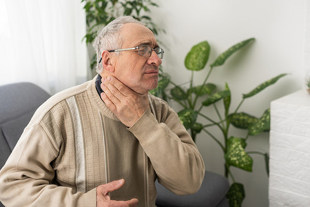 牙痛的老人坐在家里的沙发上摸着脸颊疼痛。